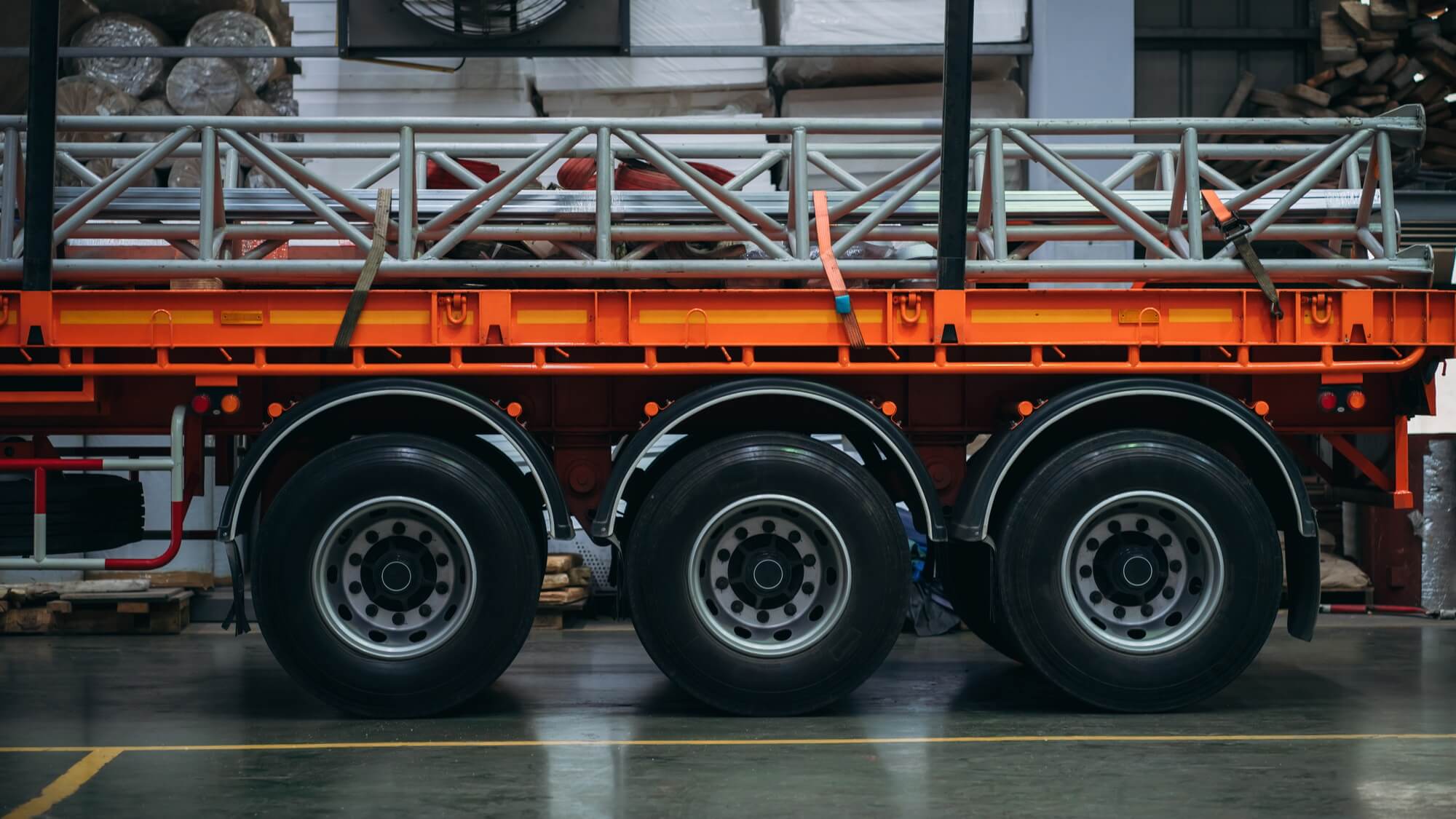 A large orange semi truck with three wheels and a trailer